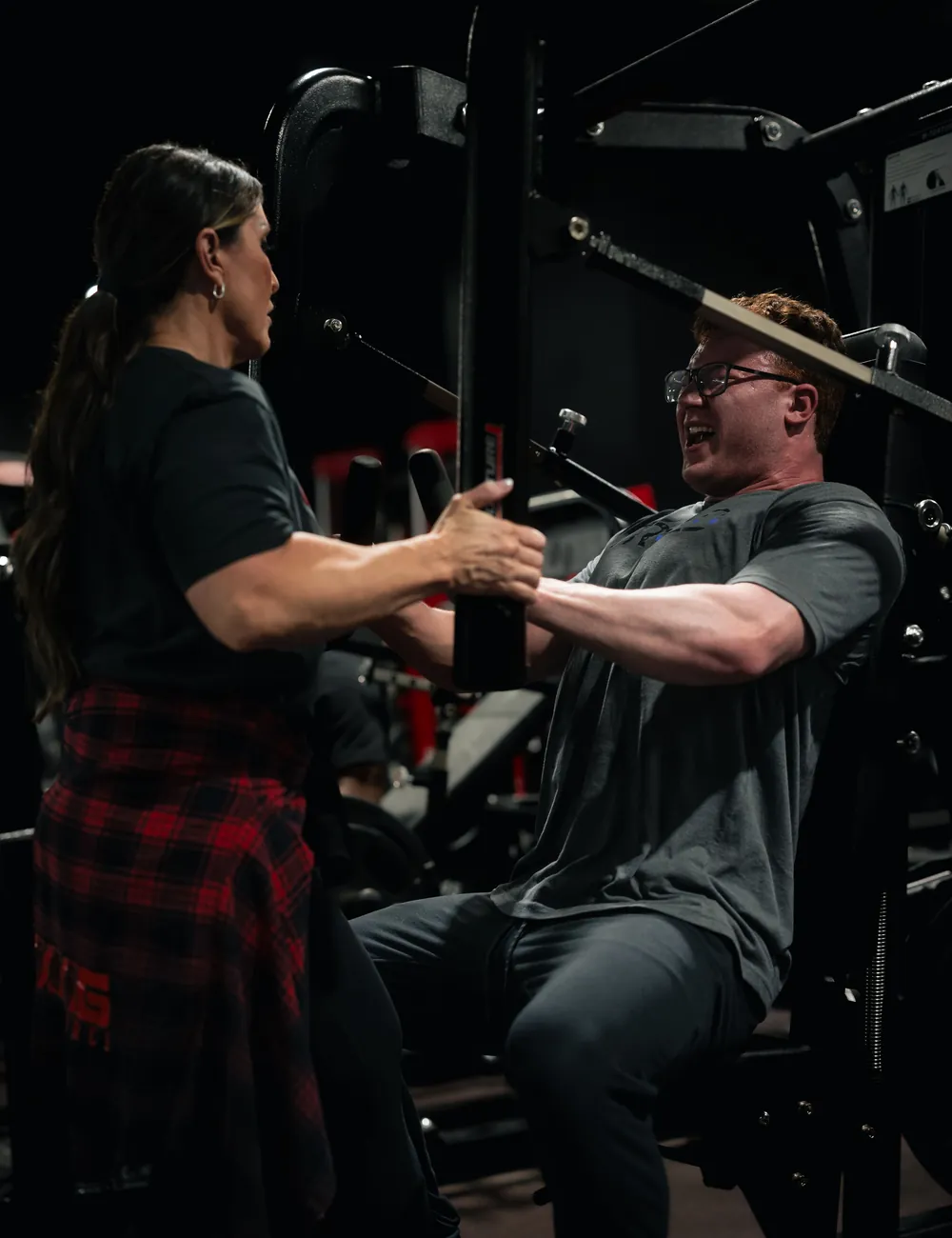 Personal trainer coaching a client through a machine chest press in a dark strength studio