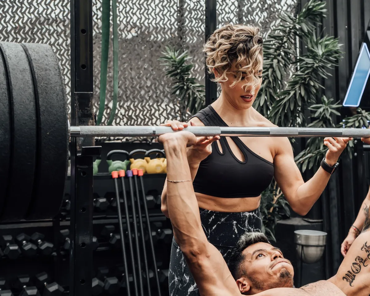 Coach spotting a client's barbell bench press in a strength studio